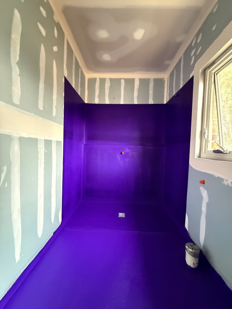 Full shower recess with purple waterproofing membrane applied to floor and three walls up to height, waste set in floor — Keysborough job by Casey Quality Coatings