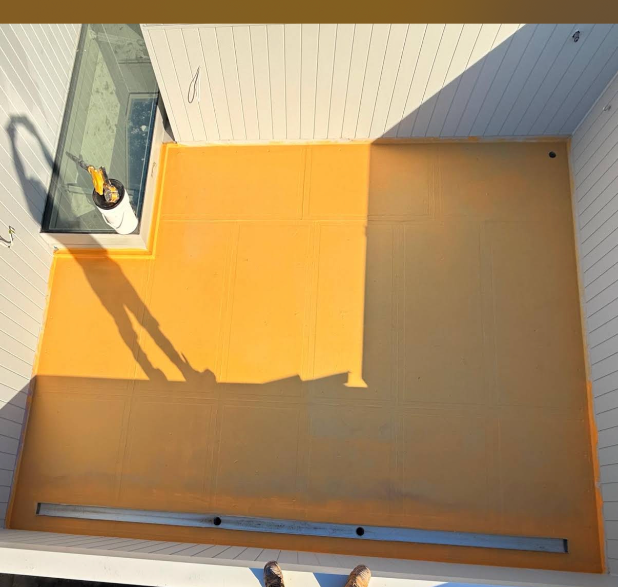 Overhead view of full balcony deck with yellow waterproofing membrane being applied, linear drain at base, skylight junction detailed and white cladded walls — Mount Waverley residential new build by Casey Quality Coatings