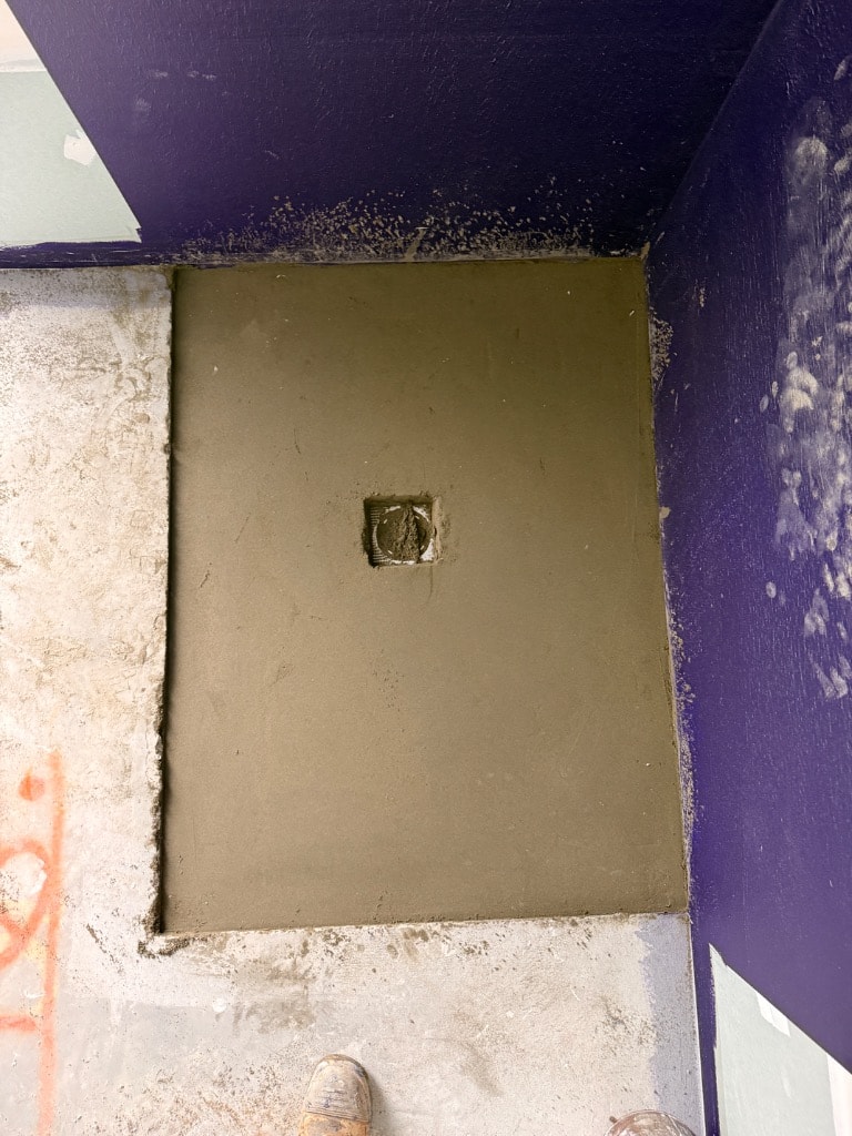 Fresh screed being laid on shower base with purple waterproofed walls — Mount Waverley job by Casey Quality Coatings