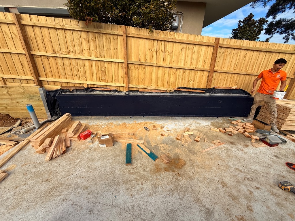 Black waterproofing membrane fully applied to retaining wall face on residential construction site — Mount Waverley job by Casey Quality Coatings