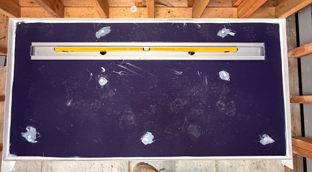 Overhead view of shower base with purple waterproofing membrane fully applied, linear drain installed and spirit level confirming correct fall — Narre Warren job by Casey Quality Coatings